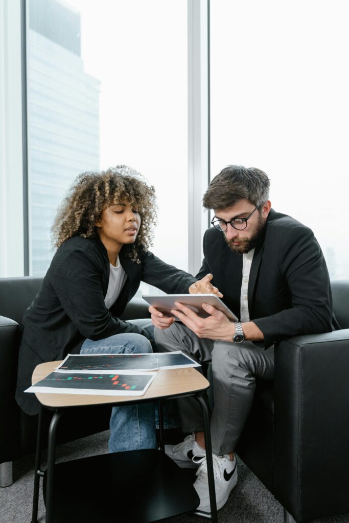 Two colleagues analyzing financial data and charts indoors using a digital tablet.